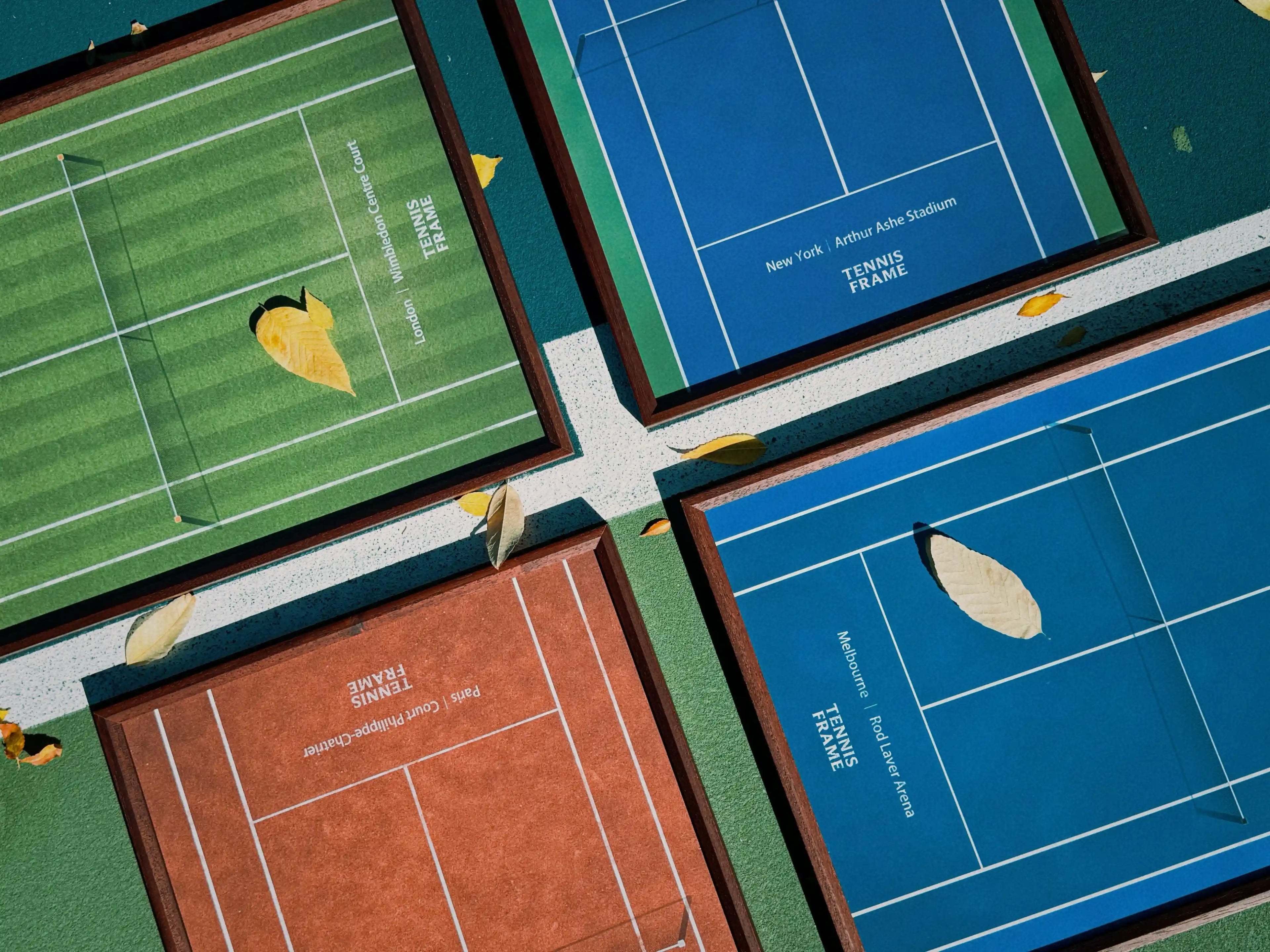Grand Slam Tennis Frame collection—Wimbledon, US Open, French Open, and Australian Open—angled flat lay on a tennis court with fall leaves