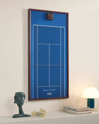 Angled view of the Melbourne Summer Blue empty tennis racket display frame with a walnut wood frame, brass hook, and premium blue hard court background in a modern interior.