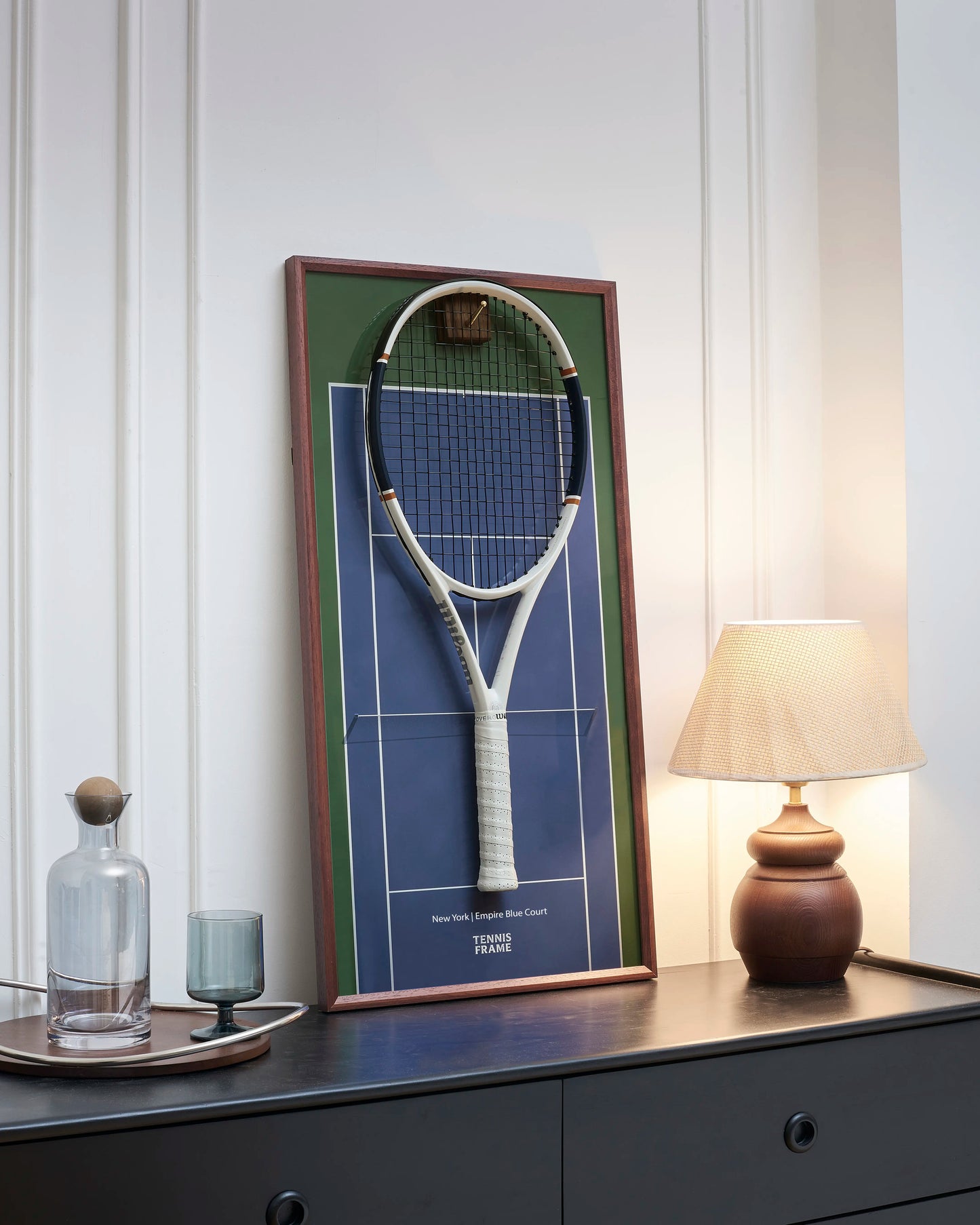 TENNIS FRAME Angled view of the New York Empire Blue Court tennis racket display frame with a mounted racket, featuring a walnut wood frame, brass hook, and premium home decor styling. 