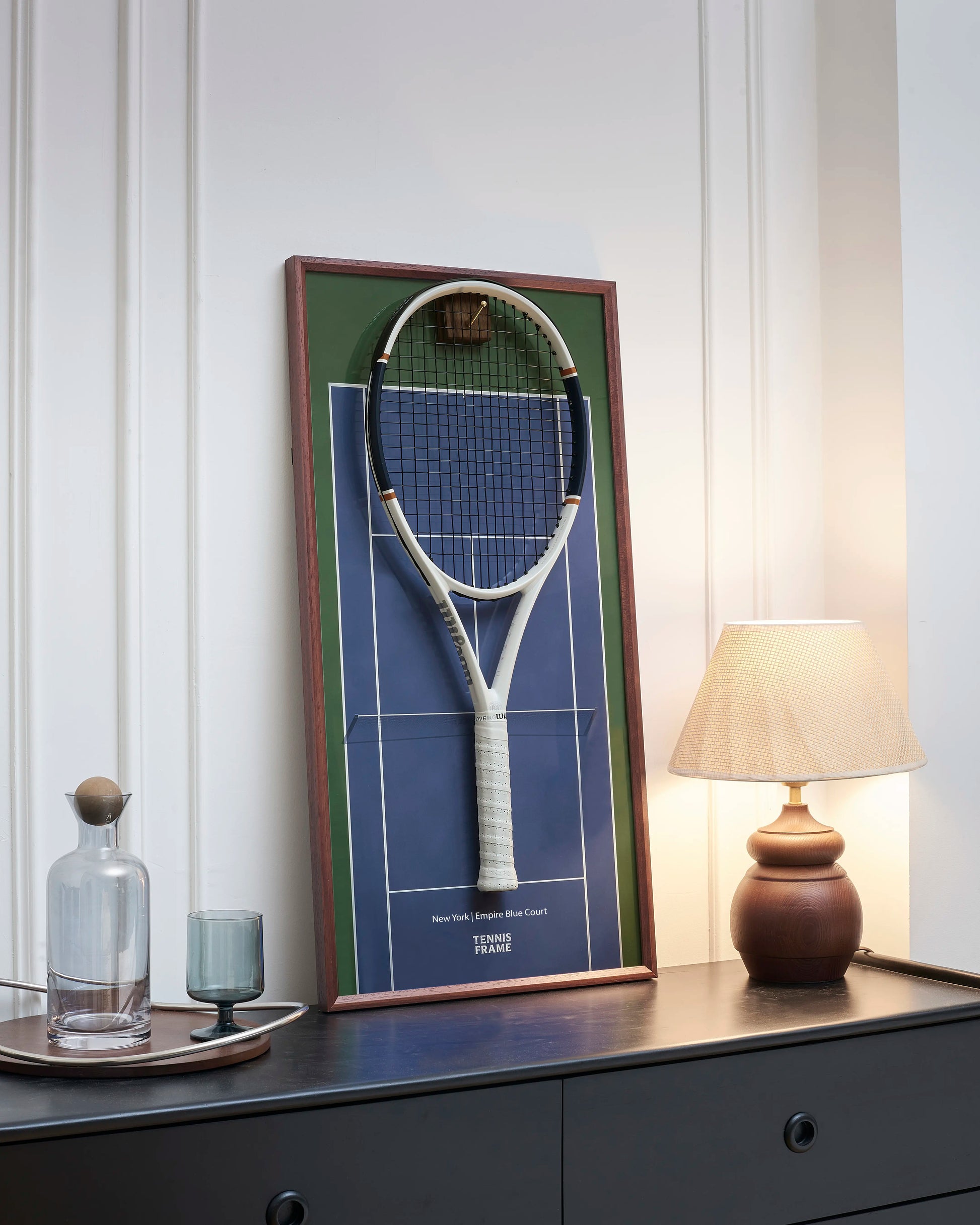 TENNIS FRAME Angled view of the New York Empire Blue Court tennis racket display frame with a mounted racket, featuring a walnut wood frame, brass hook, and premium home decor styling. 