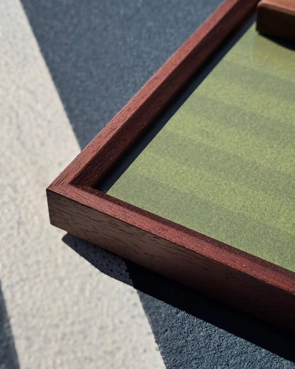 Walnut wood tennis frame corner detail in natural light, showing rich grain and grass court background texture