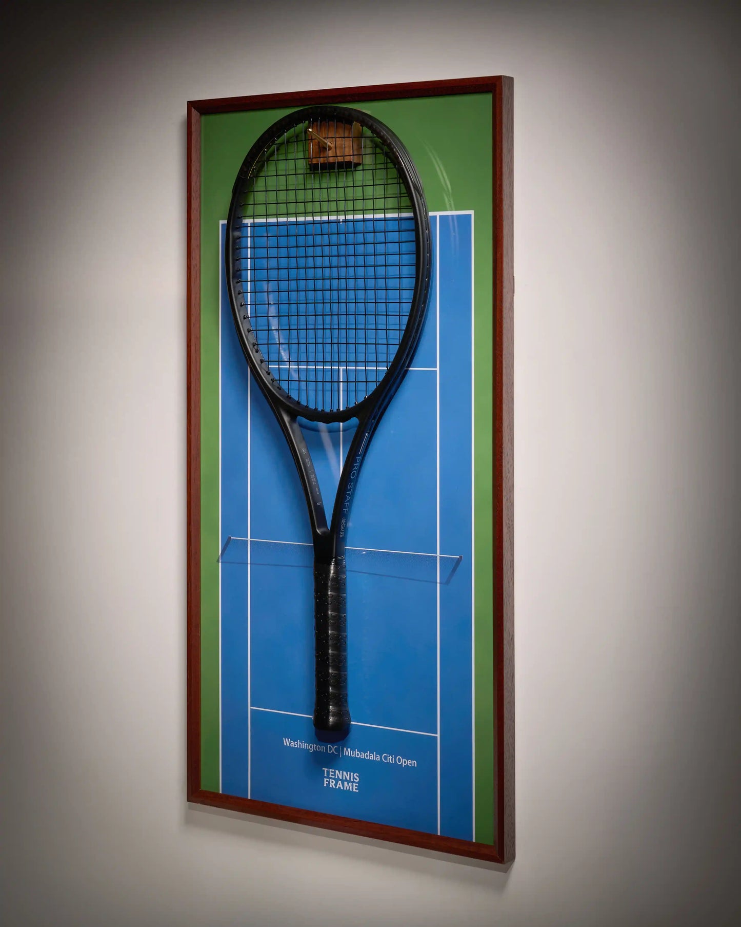 Washington DC Mubadala Citi Open tennis racket display frame with blue hard-court background, green outer lanes, walnut frame and hook, side angle view with mounted black racket
